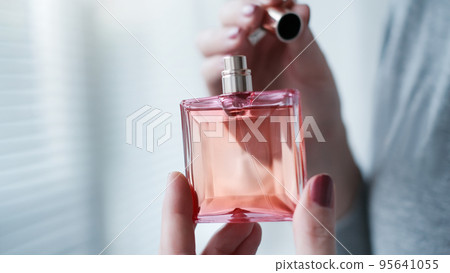 Perfume bottle in a female hand against the background of light room interior. Perfume bottle in a female hand against the background of light room interior. 95641055