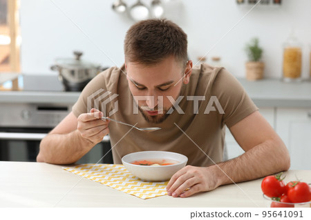 Young man eating tasty vegetable soup at table in kitchen 95641091