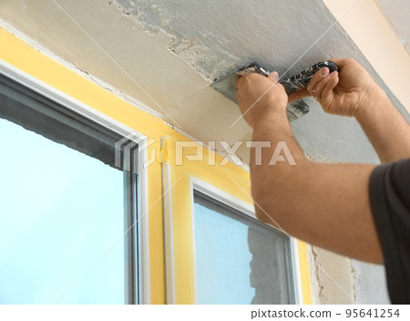Man plastering window area with putty knife indoors, closeup. Interior repair Man plastering window area with putty knife indoors, closeup. Interior repair 95641254