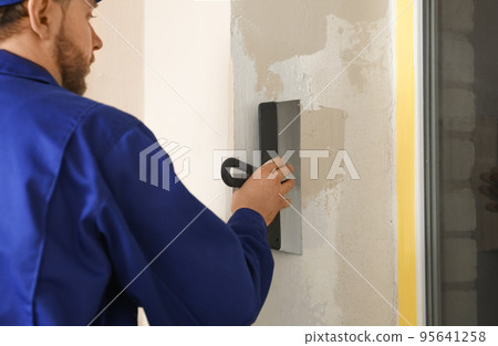 Professional worker plastering window area with putty knife indoors, closeup. Interior repair 95641258