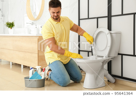 Young man feeling disgust while cleaning toilet bowl in bathroom Young man feeling disgust while cleaning toilet bowl in bathroom 95641364