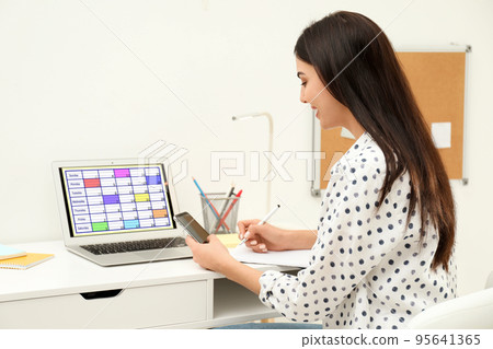 Young woman planning her schedule with calendar app on laptop in office Young woman planning her schedule with calendar app on laptop in office 95641365