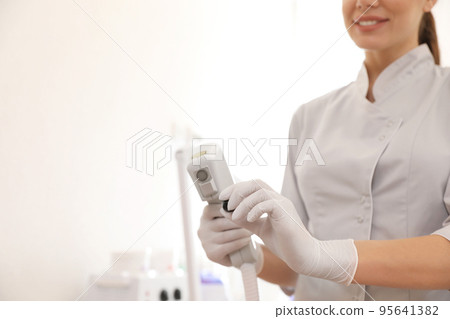 Young woman holding professional laser epilator in beauty salon, closeup. Space for text 95641382