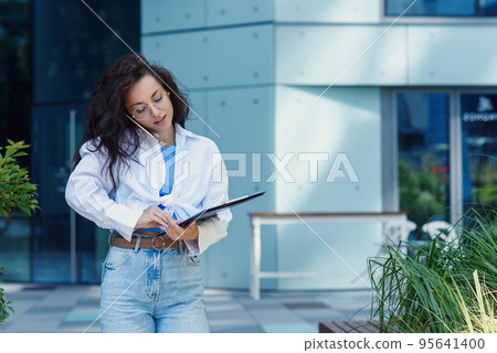 Successful beautiful business woman in suit with document walking to the meeting near modern office building. Successful beautiful business woman in suit with document walking to the meeting near modern office building. 95641400