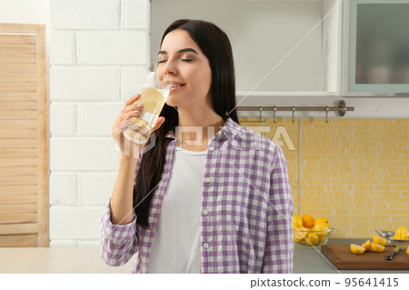 Beautiful young woman drinking lemon water in kitchen 95641415