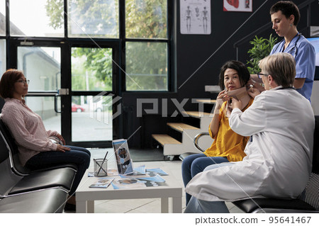 Injured patient removing neck collar with medic and assistant, receiving help during examination. Woman wearing cervical brace to recover after accident injury, doing checkup at health clinic 95641467