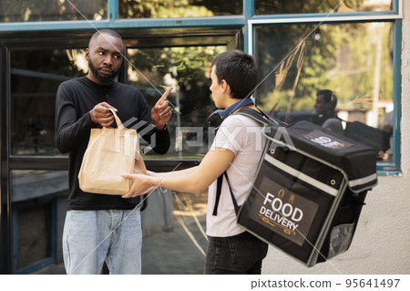 Unsatisfied client refuse taking food order, bad delivery service, courier and angry customer. Woman giving upset employee takeaway meal near office building outdoors, medium shot Unsatisfied client refuse taking food order, bad delivery service, courier and angry customer. Woman giving upset employee takeaway meal near office building outdoors, medium shot 95641497