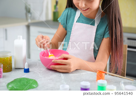 Little girl mixing ingredients with silicone spatula at table in kitchen, closeup. DIY slime toy 95641540