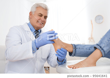 Male orthopedist checking patient's foot in clinic 95641641