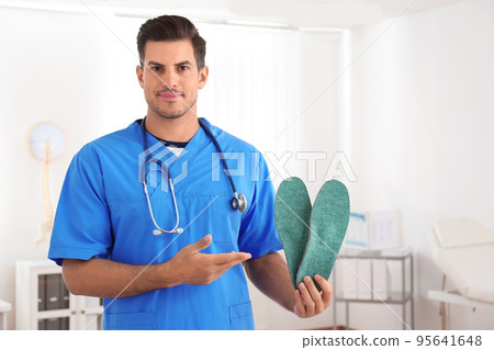 Handsome male orthopedist showing insoles in clinic 95641648