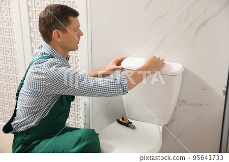 Professional plumber repairing toilet bowl in bathroom 95641733