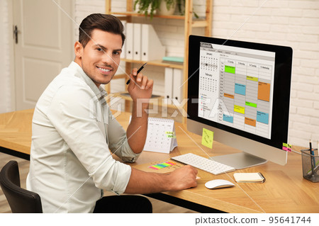 Handsome man using calendar app on computer in office Handsome man using calendar app on computer in office 95641744