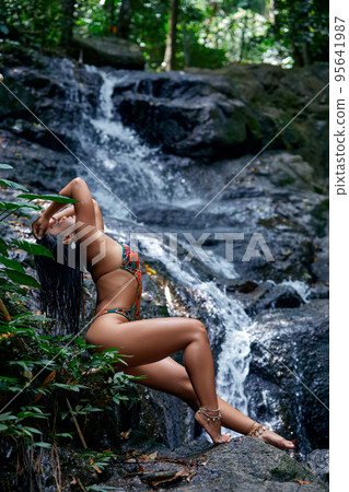 Beautiful woman posing at small tropical waterfall Beautiful woman posing at small tropical waterfall 95641987