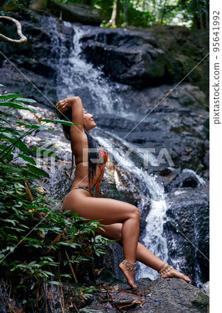 Beautiful woman posing at small tropical waterfall Beautiful woman posing at small tropical waterfall 95641992