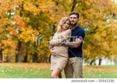 Young pregnant woman and her handsome husband are walking at the autumn park. 95642286