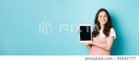 Image of happy young girl showing digital tablet screen and smiling proud, showing your logo on display, standing over blue background Image of happy young girl showing digital tablet screen and smiling proud, showing your logo on display, standing over blue background 95642777