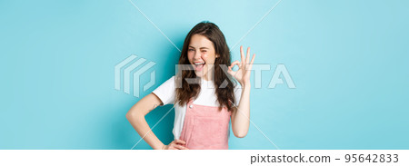 Image of cheerful glamour woman winking and showing OK sign to recommend and approve nice thing, like and agree, saying yes, praising good choice, blue background Image of cheerful glamour woman winking and showing OK sign to recommend and approve nice thing, like and agree, saying yes, praising good choice, blue background 95642833