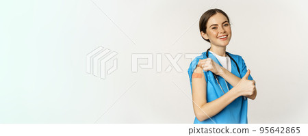 Happy smiling medical worker, doctor or nurse showing her shoulder after vaccination, covid-19 vaccine and thumbs up satisfied, standing over white background 95642865