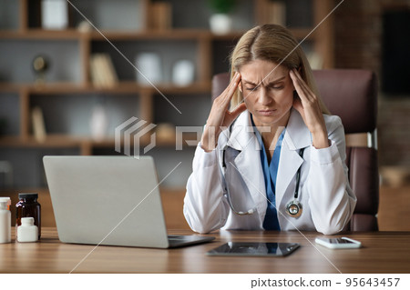 Portrait Of Stressed Female Doctor In Uniform Suffering Headache At Workplace 95643457