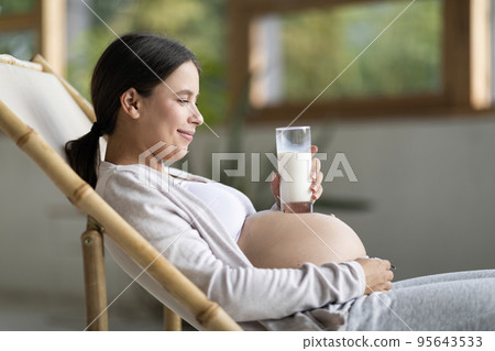 Smiling Young Woman Placing Glass With Milk On Her Pregnant Belly 95643533