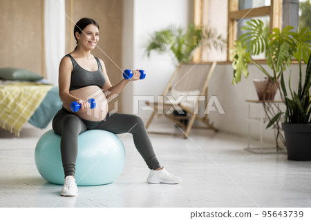 Smiling Pregnant Female Training With Dumbbells And Sitting On Fitball At Home Smiling Pregnant Female Training With Dumbbells And Sitting On Fitball At Home 95643739