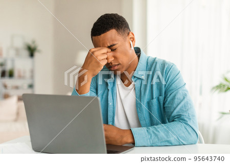 Despaired tired millennial black man resting from work with laptop, suffering from migraine and stress Despaired tired millennial black man resting from work with laptop, suffering from migraine and stress 95643740