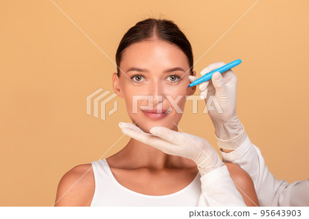 Lady before plastic surgery operation. Beautician touching and drawing correction lines on female face 95643903