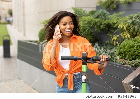 Smiling millennial african american female in casual calling by smartphone, talk with friend on city street Smiling millennial african american female in casual calling by smartphone, talk with friend on city street 95643965