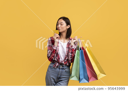 Time for shopping. Young asian female customer holding colorful shopper bags and kissing debit credit card, copy space Time for shopping. Young asian female customer holding colorful shopper bags and kissing debit credit card, copy space 95643999