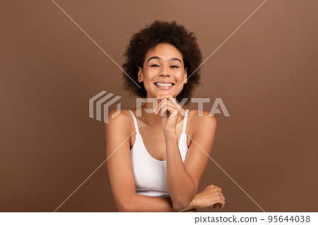 Smiling pretty young mixed race woman with curly hair and perfect face, looking at camera on brown background Smiling pretty young mixed race woman with curly hair and perfect face, looking at camera on brown background 95644038