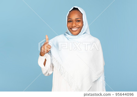 Happy african american muslim woman showing thumb up on blue studio background, recommending product, service, purchase 95644096