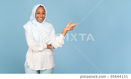 Look there. Happy black muslim lady pointing finger aside at copy space over blue background, showing place for your ad 95644131
