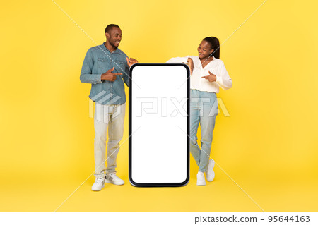 Black Couple Pointing At Big Smartphone Blank Screen, Studio Shot Black Couple Pointing At Big Smartphone Blank Screen, Studio Shot 95644163