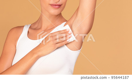 Hyperhidrosis concept. Closeup of young lady wiping her under arm area with napkin towel, standing on beige background Hyperhidrosis concept. Closeup of young lady wiping her under arm area with napkin towel, standing on beige background 95644187