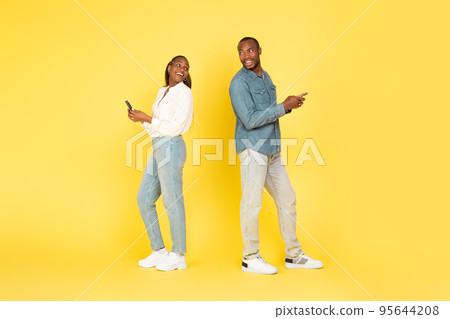 Black Couple Using Phones Smiling To Each Other, Yellow Background Black Couple Using Phones Smiling To Each Other, Yellow Background 95644208