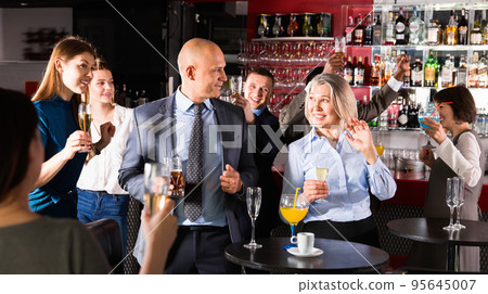 Cheerful middle aged woman with male colleague enjoying office party in bar, talking and toasting with drinks 95645007