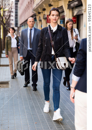 Stylish young business woman in casual dress walking through city street in crowd of people Stylish young business woman in casual dress walking through city street in crowd of people 95645123
