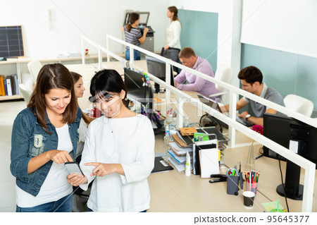 Asian and European girls using their smartphones in open space office 95645377