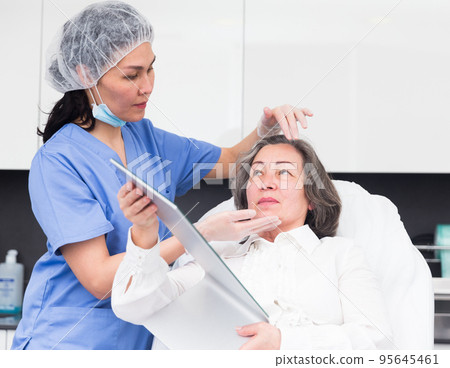 Female cosmetologist examining face skin of elderly woman Female cosmetologist examining face skin of elderly woman 95645461