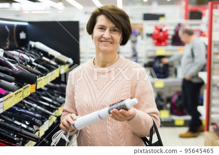 Middle aged woman choosing curling iron brush in appliance shop Middle aged woman choosing curling iron brush in appliance shop 95645465
