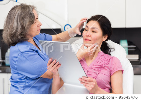 Cosmetologist explaining female client future hardware facial procedure Cosmetologist explaining female client future hardware facial procedure 95645470