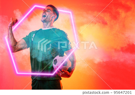 Caucasian male player with soccer ball screaming over illuminated hexagon against neon background 95647201