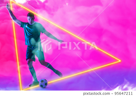 Caucasian male player playing with ball over illuminated triangle against pink neon background 95647211