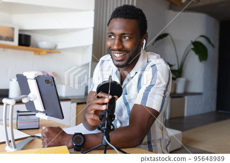 Happy african american man sitting at table in kitchen, using tablet and making vlog 95648989