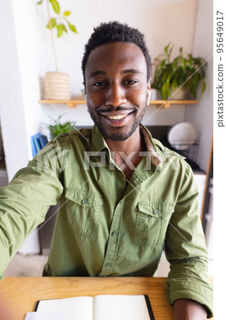 Happy african american man sitting at table in kitchen, having video call 95649017