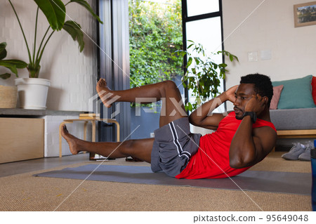 African american man exercising in living room, using tablet African american man exercising in living room, using tablet 95649048