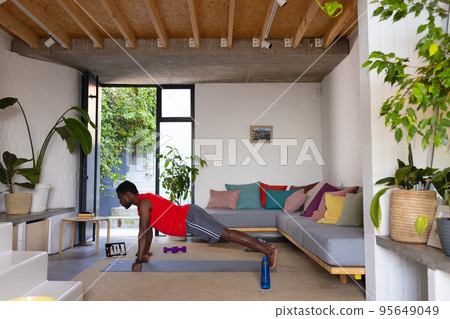 African american man exercising in living room, using tablet African american man exercising in living room, using tablet 95649049