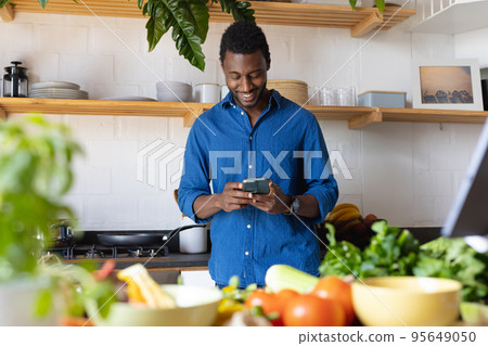 Happy african american man cooking dinner in kitchen, using smartphone Happy african american man cooking dinner in kitchen, using smartphone 95649050