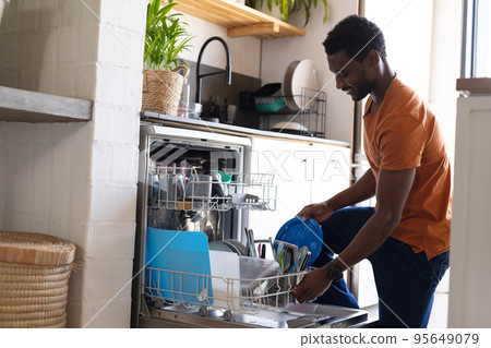 Happy african american man standing in kitchen and unloading dishwasher 95649079