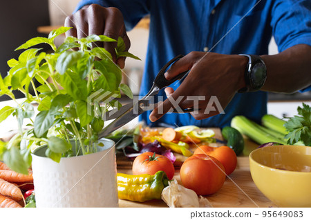 Midsection of african american man standing in kitchen and cooking dinner 95649083
